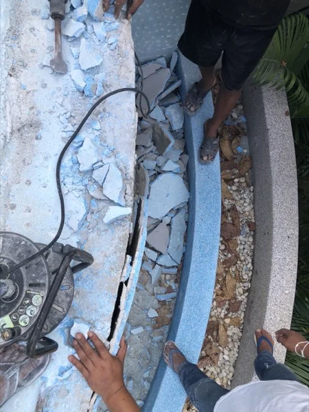 The old surround being cut off in a strip along the curved edge of the pool