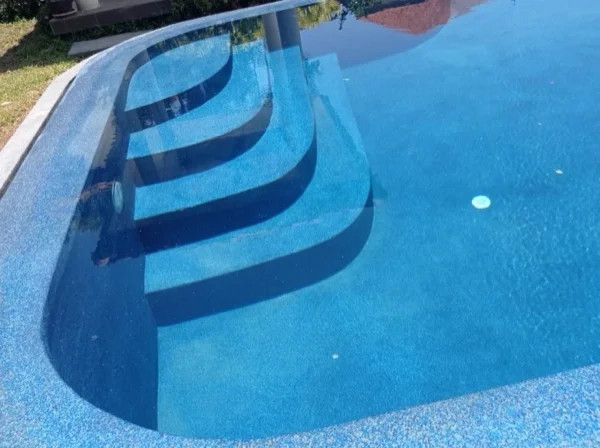 The entry steps of the renovated pool seen through the water, in PebbleCrete Glass Riviera Pearl