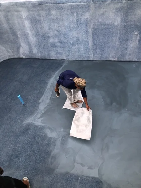 Working the surface of the pool floor by hand once the new fittings were in