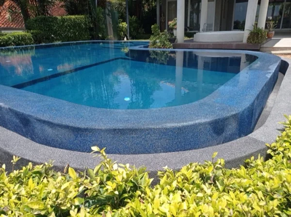 The renovated pool finished in PebbleCrete Glass Riviera Pearl, seen from the garden with the villa behind