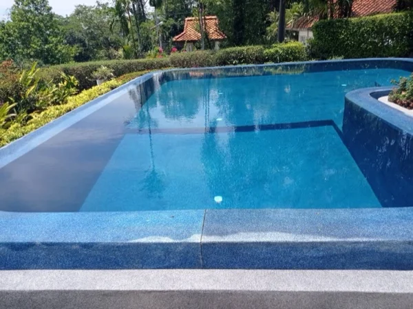 The raised spillway wall at the far side of the pool, finished in Riviera Pearl with a dark speckled coping