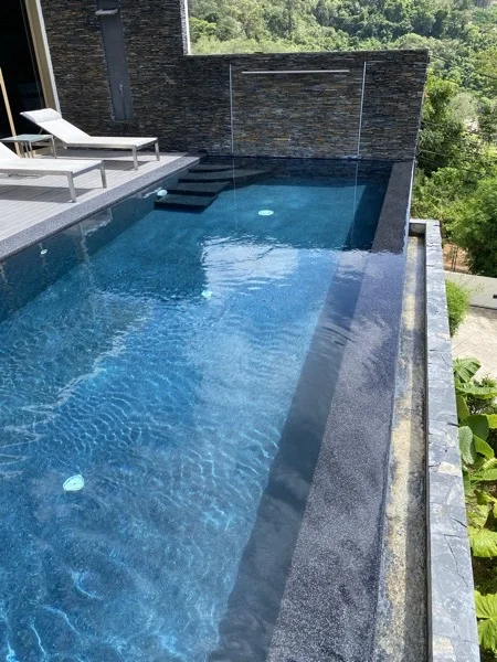 The length of the pool beside the stone-clad wall: entry steps and a submerged sun ledge in Nightfall Pearl against the Royal Blue interior