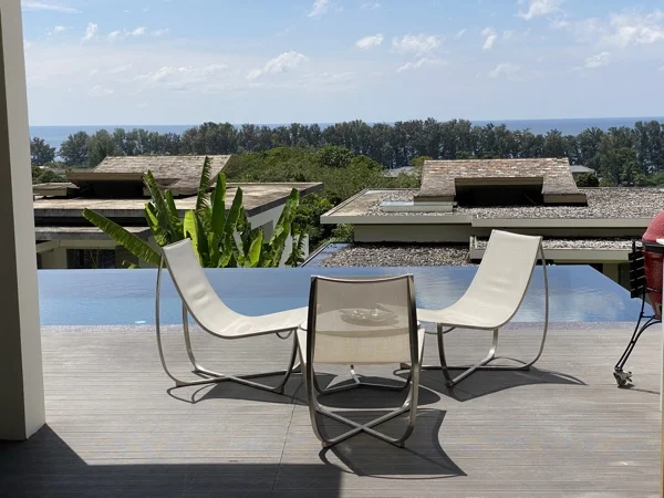 Loungers and a table on the timber terrace beside the finished pool, with the estate and the coast beyond