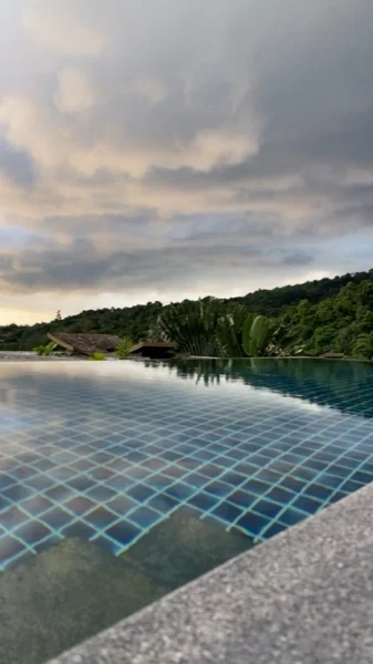 The pool before the renovation: a tiled interior with grouted joints, seen over the infinity edge at dusk