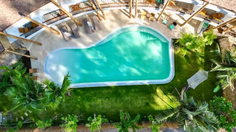 Aerial view of the curved pool at The Talay, with a pale shallow entrance beside the garden and hotel.